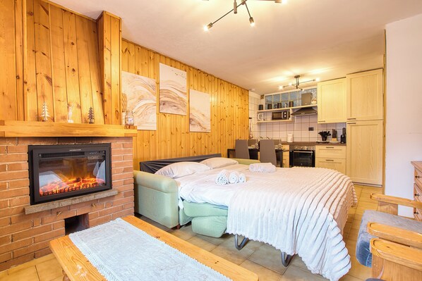 Ein gemütliches Zimmer mit Kamin, einem Bett, einer Sitzbank und einer Küchenzeile.
