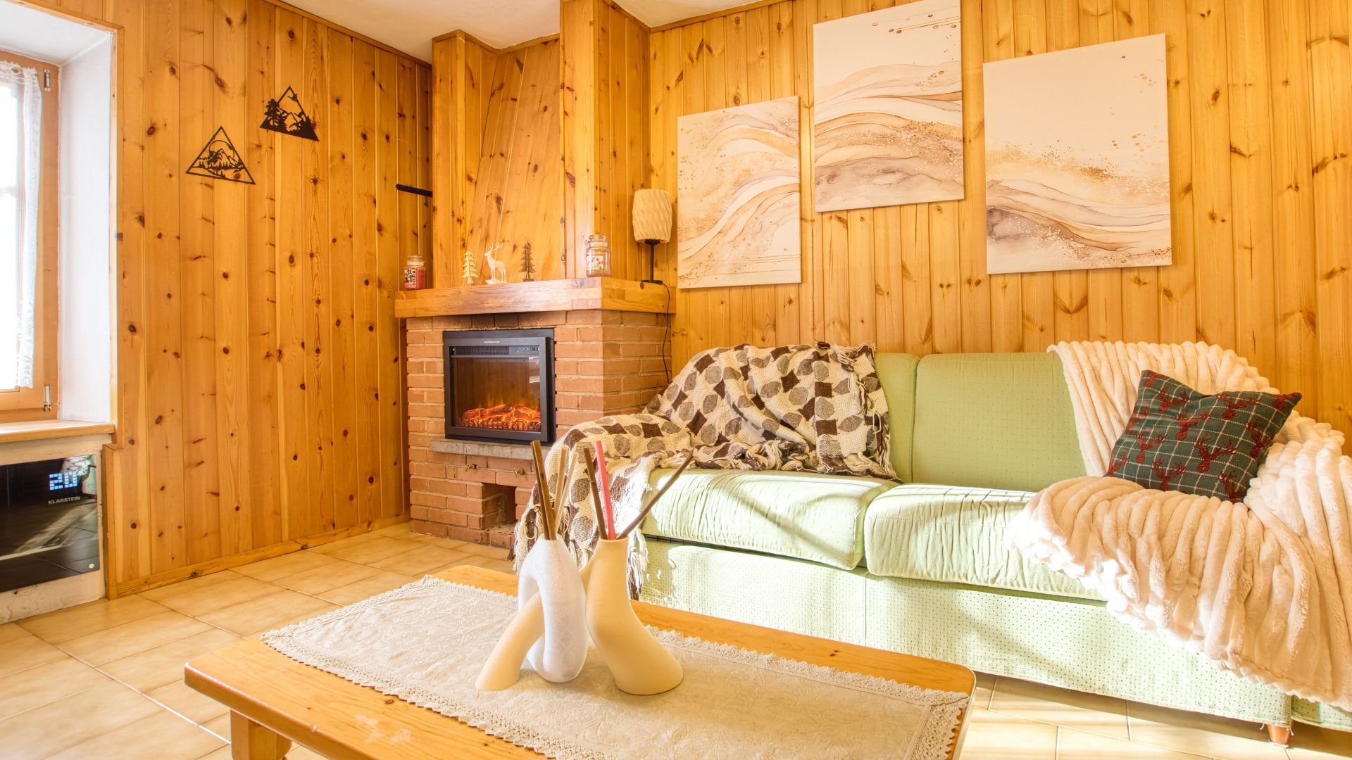 A cozy living room with a fireplace, wooden walls, a green sofa, and a white vase.