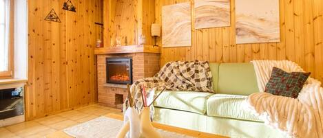 A cozy living room with a fireplace, wooden walls, a green sofa, and a white vase.