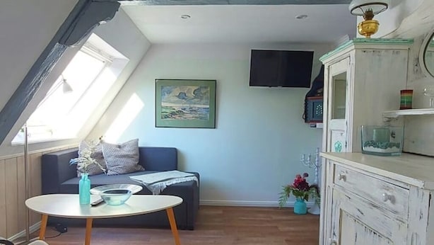 A cozy room with a sloped ceiling, a sofa, a small round table, and a cabinet with decorative items. - Lütt Stuuv im historischen Flensburger Hafen (Flensburg)