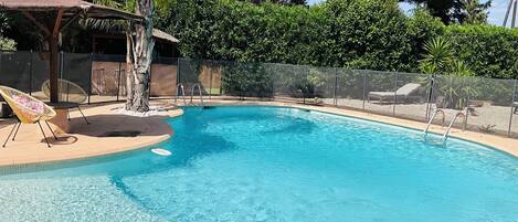 A swimming pool with clear blue water, surrounded by a fence, and shaded by trees.