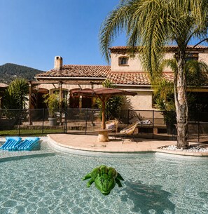 Una piscina con un flotador con forma de cocodrilo, un área de patio techada y un edificio con tejado de tejas.