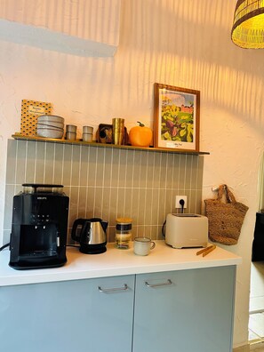 Une cuisine équipée d’une machine à café, d’un grille-pain, d’une bouilloire et d’un tableau encadré au mur.