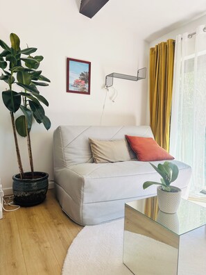 A living room with a sofa, a potted plant, a framed picture, and a window with curtains. - 4-Star Suite - Garden, Pool, Small Events Available (Solliès-Pont)