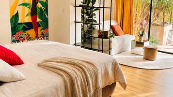 Un dormitorio con cama, sofá, estantería de plantas y vistas por un amplio ventanal.