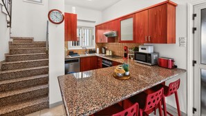 A modern kitchen with granite countertops, red cabinets, and a central island with bar stools. - Rock Azure Villa | Pool & Jacuzzi in Ayia Thekla (Ayia Napa)