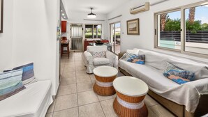 A modern living room with a sofa, two wicker side tables, and a dining area with a table and chairs. - Rock Azure Villa | Pool & Jacuzzi in Ayia Thekla (Ayia Napa)