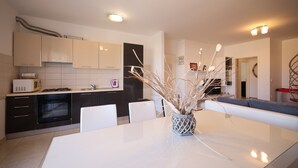 A modern kitchen with white cabinets, a built-in oven, and a dining area with a white table and chairs. - Apartment Skroce (Zaton)