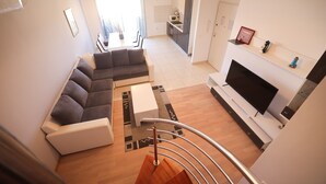 A modern living room with a sofa, a coffee table, and a TV. There is a staircase leading to another level. - Apartment Skroce (Zaton)