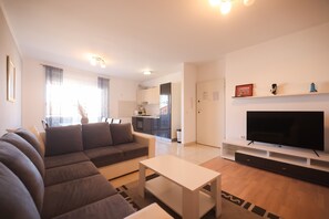 Een moderne woonkamer met een grijze bank, een witte salontafel en een flatscreen televisie op een witte kast.