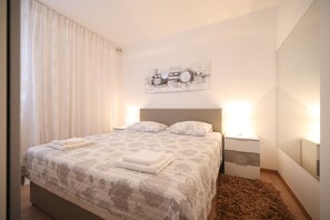 Een moderne slaapkamer met een groot bed, een nachtkastje, en een wandlamp.