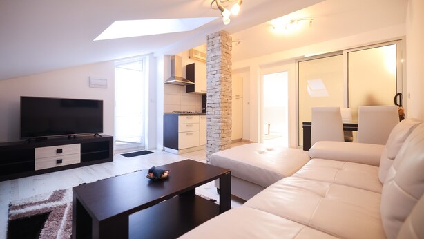 A modern living room with a flat-screen TV, a dark coffee table, a white sofa, and a stone pillar. - Apartment Skroce (Zaton)