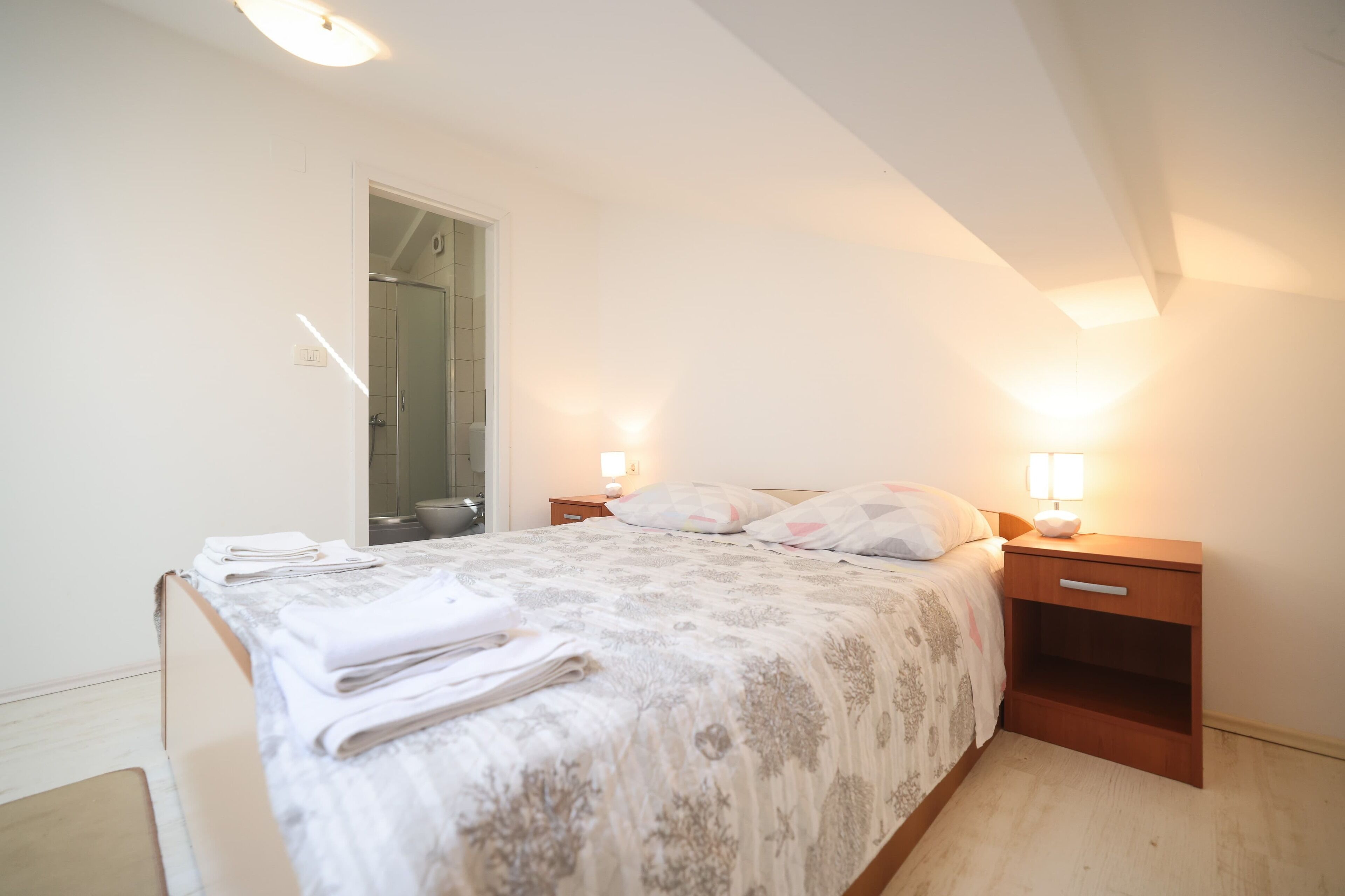 A bedroom with a bed, bedside tables, a nightstand, a mirror, and a door.