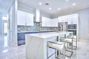 A modern kitchen with white cabinets, a marble island, and stainless steel appliances. - Bergamo 4BR Pool Home | Hot Tub & Ping Pong (Naples)