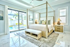 A bedroom with a four-poster bed, a bench, a nightstand, a lamp, and a view of a swimming pool. - Bergamo 4BR Pool Home | Hot Tub & Ping Pong (Naples)