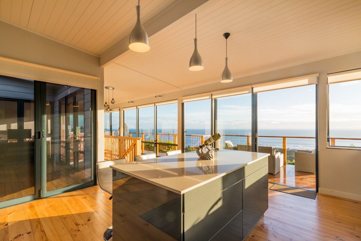 A modern interior with a large island, wooden flooring, and a view of the sea.