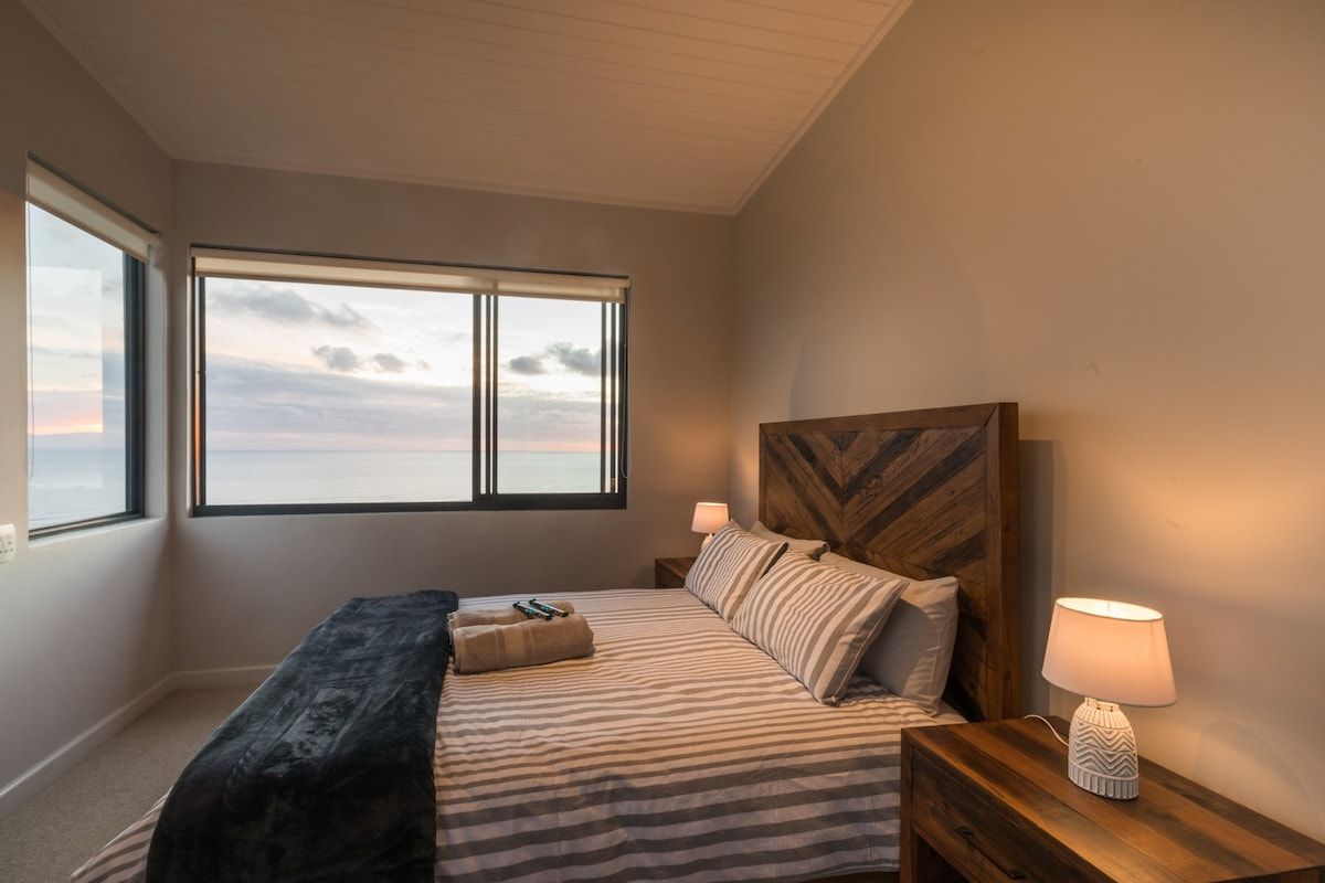 A bedroom with a large window, a bed with striped bedding, a wooden headboard, and two bedside lamps.
