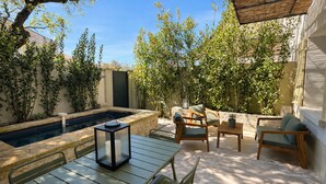 Een terras met een zwembad, tuinmeubilair en weelderige begroeiing.