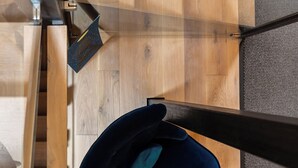 Een houten trap met glazen leuningen en een donkerblauwe stoel onderaan.