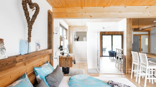 Een gezellige kamer met een houten plafond, een bed met opvallende kussens, een decoratie in de vorm van een hart, en uitzicht op een eetgedeelte.