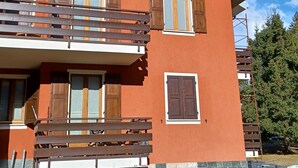 Un immeuble à plusieurs étages, doté de volets en bois aux fenêtres, d’un balcon et d’une base en pierre.