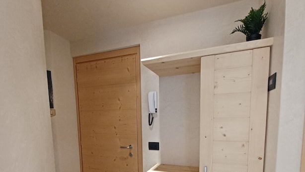 Un couloir avec une porte en bois, un meuble en bois doté de tiroirs et une petite plante posée sur le dessus.