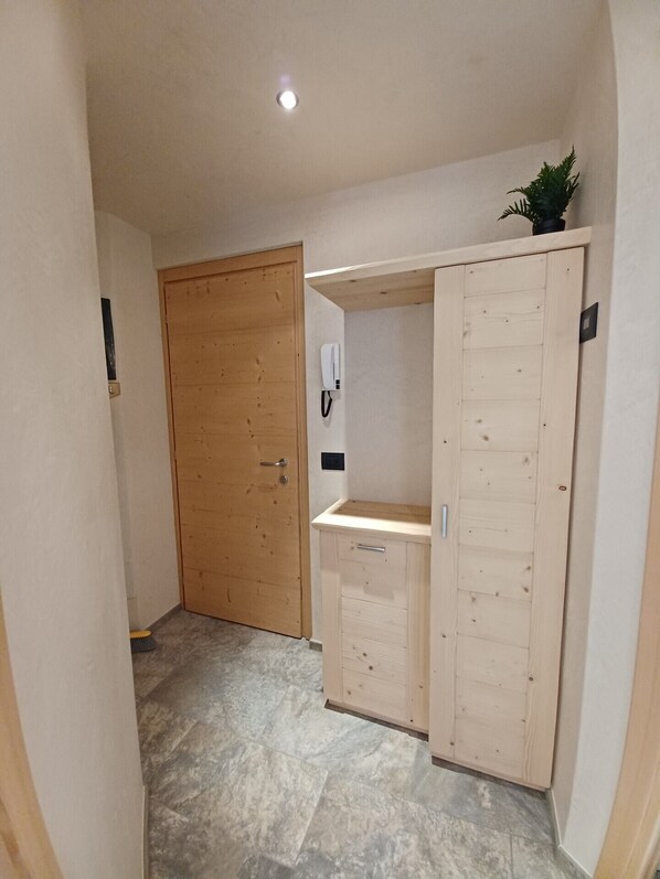 A hallway with a wooden door, a wooden cabinet with drawers, and a small plant on top. - Two-room apartment on the second floor 500mt from the historic center of Bormio. (Bormio)
