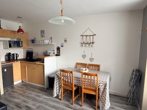 A compact kitchen with a microwave, toaster, and coffee maker. There is a dining table with four chairs and a patterned tablecloth.