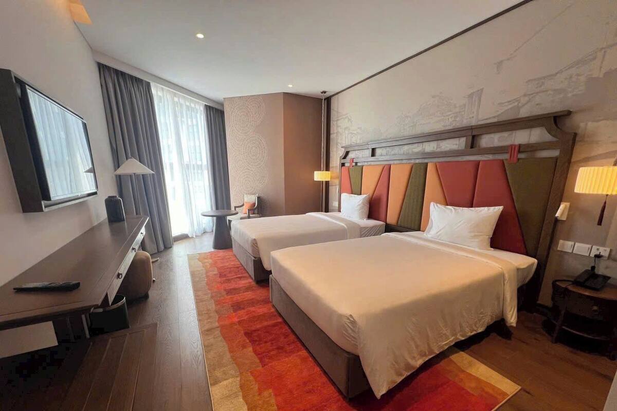 A hotel room with two beds, a desk, and a TV.