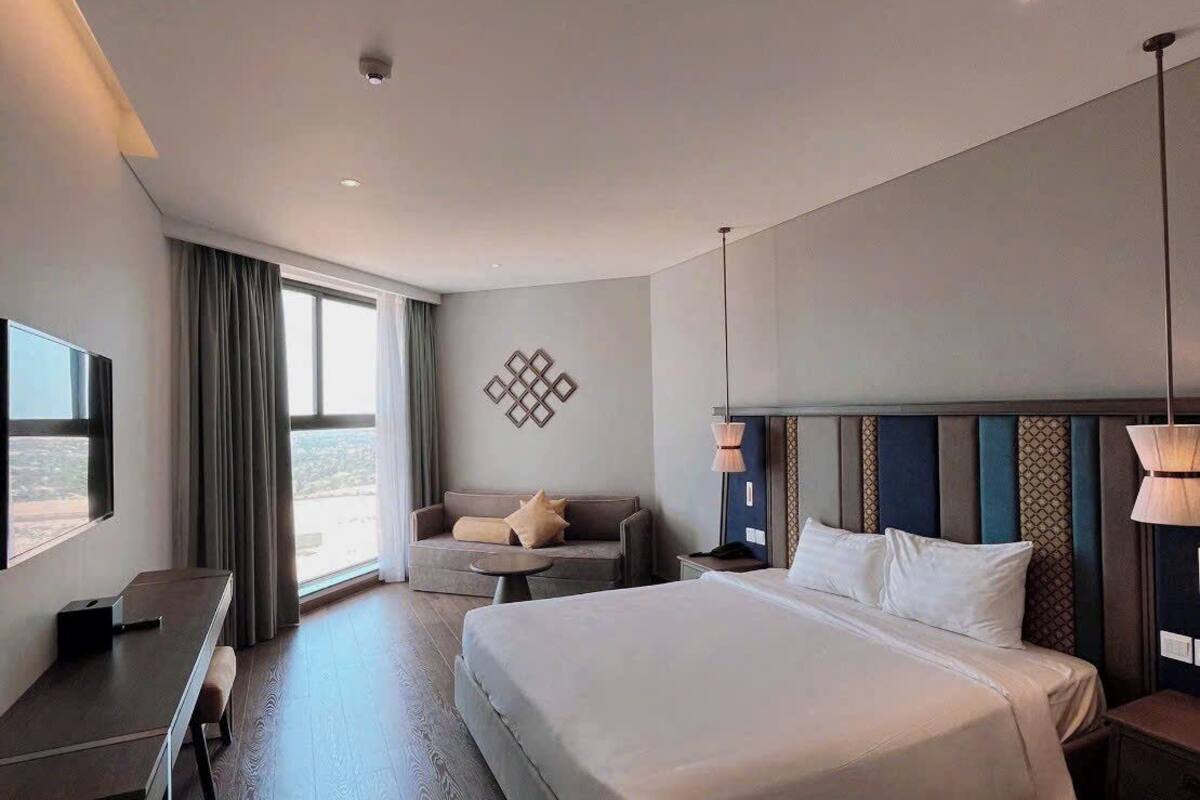 A modern hotel room with a large bed, a desk, and a sofa.
