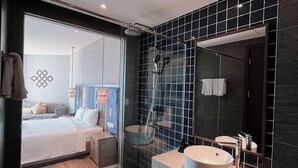 Una camera d'albergo moderna con un letto grande, box doccia in vetro, una toeletta con uno specchio ampio e vista sulla città.