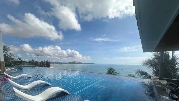 Una piscina a sfioro con vista sull'oceano, sedie a sdraio e un solarium piastrellato.