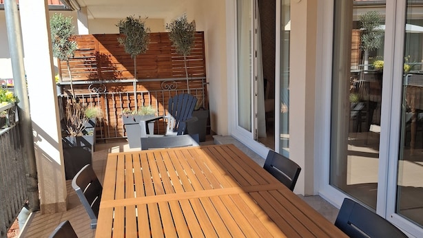 An outdoor patio with a wooden table and chairs, a wooden fence, and a view of the street. - Gîte Le Schopf - 3 bedrooms - free parking - 25 km from Strasbourg (Scharrachbergheim-Irmstett)