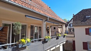 A balcony with potted plants, a railing, and a building with a tiled roof. - Gîte Le Schopf - 3 bedrooms - free parking - 25 km from Strasbourg (Scharrachbergheim-Irmstett)