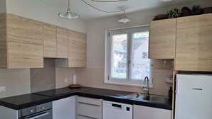 A modern kitchen with wooden cabinets, a black countertop, a built-in oven, a dishwasher, and a window with a view of buildings. - Gîte Le Schopf - 3 bedrooms - free parking - 25 km from Strasbourg (Scharrachbergheim-Irmstett)