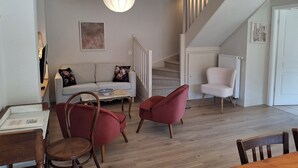 A living room with a sofa, two armchairs, a coffee table, and a dining table with chairs. A staircase leads to an upper floor. - Gîte Le Schopf - 3 bedrooms - free parking - 25 km from Strasbourg (Scharrachbergheim-Irmstett)