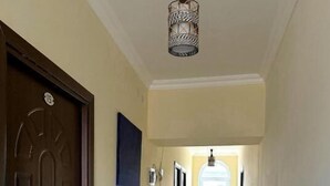 Een hal met een donker houten deur, een lichtgekleurde muur, een hangende lamp en een raam aan het einde.