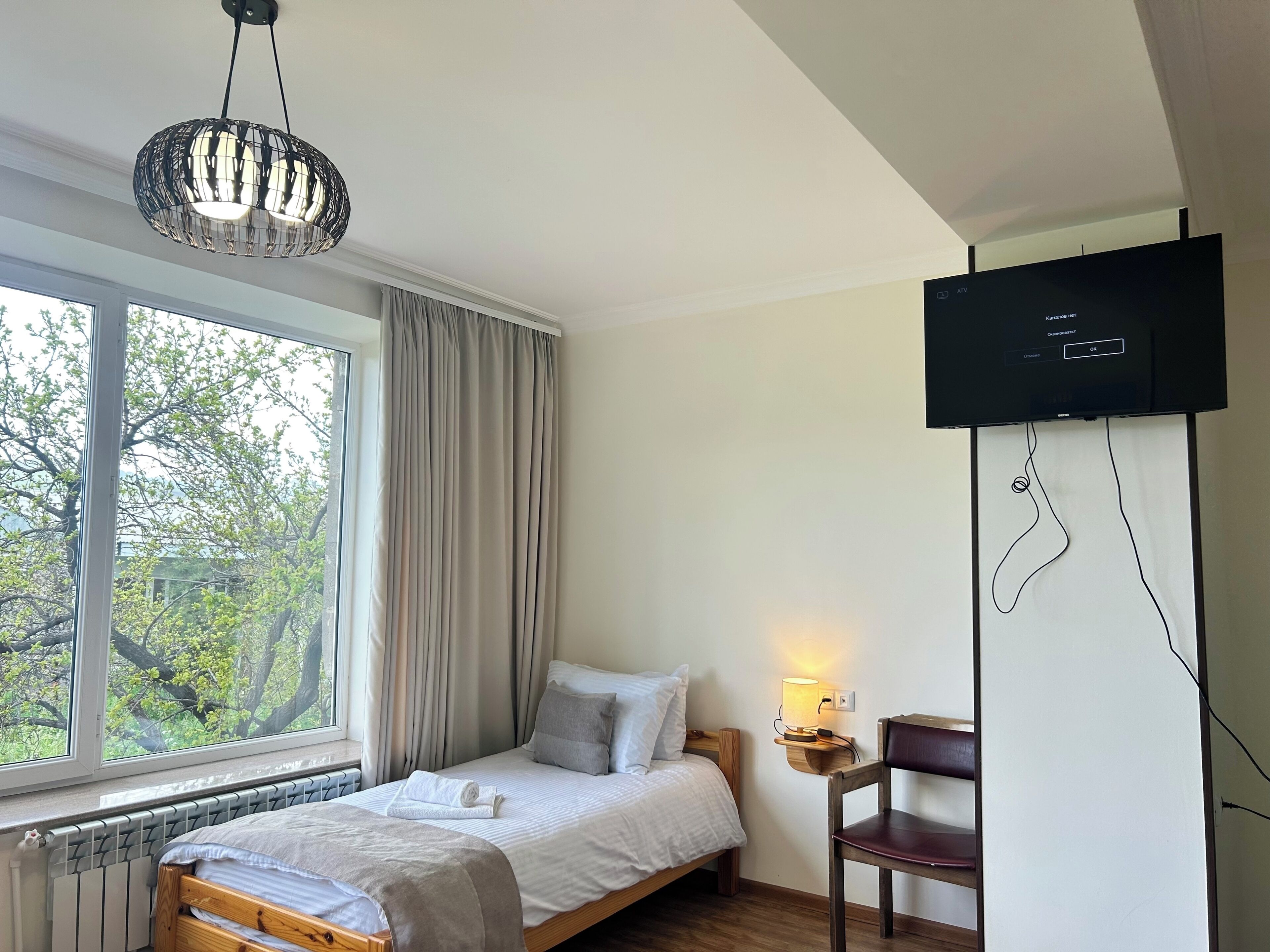 Une chambre à coucher avec un lit, une chaise, un téléviseur, une fenêtre avec des rideaux et un radiateur.
