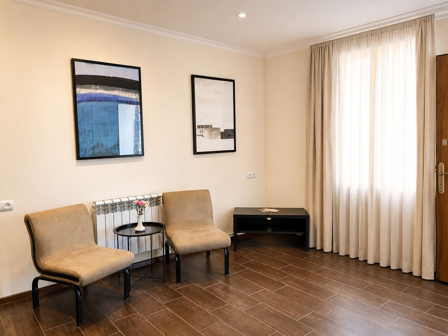 A hotel room with two armchairs, a small table, a side table, and a large window with curtains.