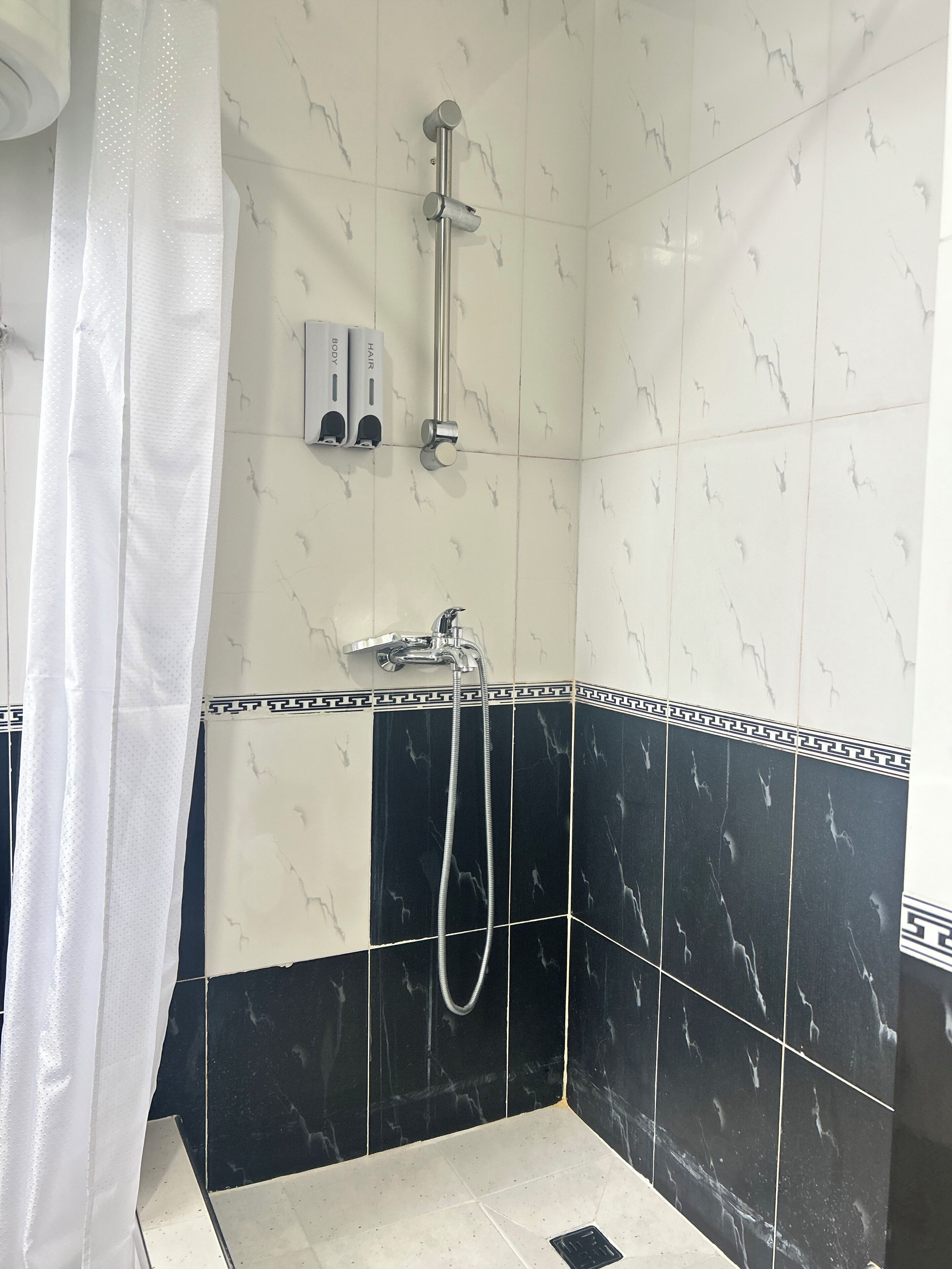 Zona de ducha con cabezal de ducha manual, llave de pared y panel de control con etiquetas 'CUERPO' y 'CABELLO'.