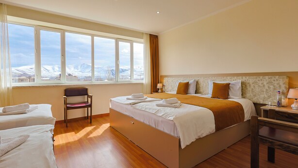 Hotelkamer met een groot bed, een stoel, een bureau en uitzicht op een besneeuwd landschap door het raam.