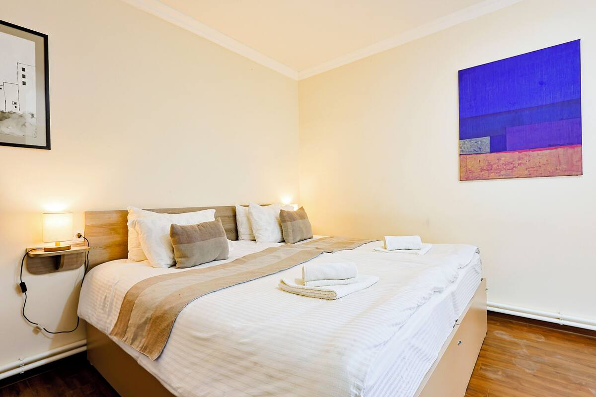 Un letto rifatto con cuscini, una lampada da comodino e un quadro appeso al muro.