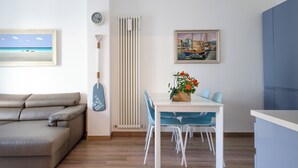 A modern living room with a sofa, a dining table with chairs, a potted plant, and a painting of a harbor scene. - SEA FRONT Gorgeous newly renovated beachfront apartment (Pesaro)