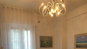 A living room with a sofa, a table, a painting, and a ceiling light fixture. - SEA FRONT Gorgeous newly renovated beachfront apartment (Pesaro)