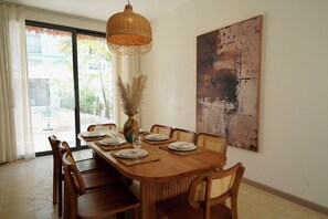A dining area with a wooden table set for six, a woven pendant light, and a large abstract painting on the wall. - Luxury 5BR Private Pool Villa in Jomtien – Perfect for Families & Groups (Muang Pattaya)