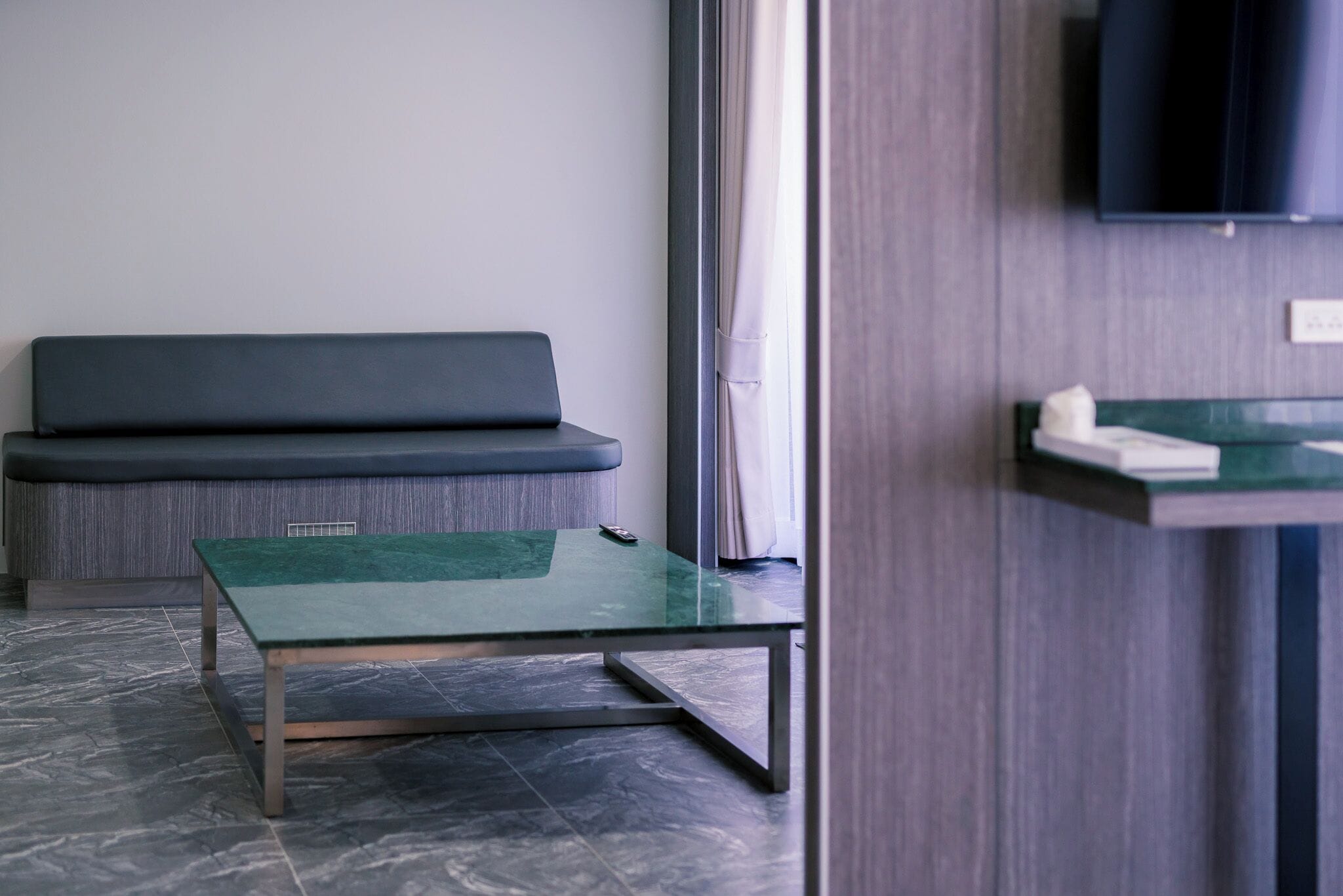 Une pièce moderne avec une table en verre vert, un canapé foncé et un téléviseur fixé au mur.