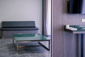 A modern room with a green glass table, a dark sofa, and a TV mounted on the wall. - One Budget Hotel Chiangrai Chiangsaen 2 (Chiang Saen)
