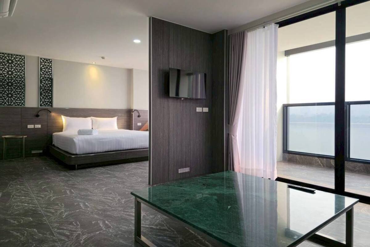A modern hotel room with a bed, a TV, a glass table, and a balcony with a view.