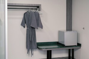 Een badkamer met een handdoekrek, een badjas, een klein wastafeltje met spiegel en een kastje.