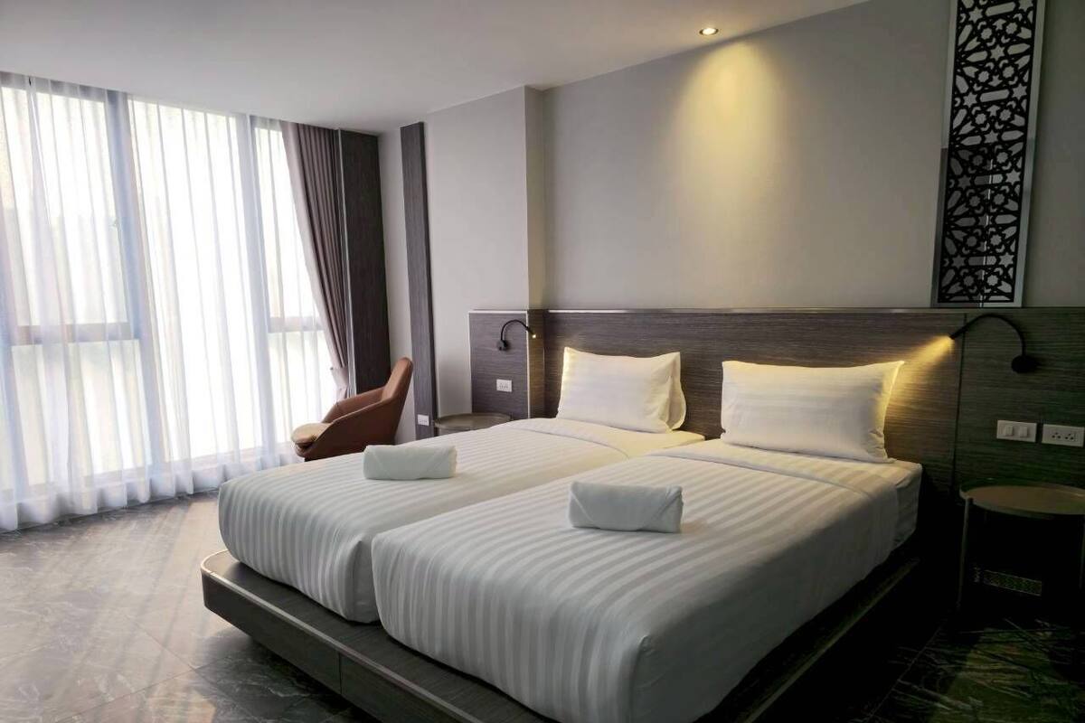 A double bed with two pillows, a chair, a bedside table, and a decorative wall panel.